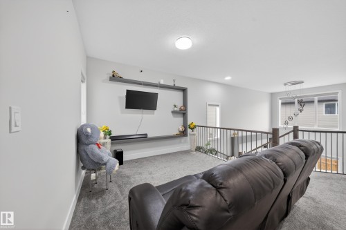 Carpeted loft area featuring a built-in entertainment unit with shelving, light gray wall paint, and a dark wood newel post with metal balusters - 449 Roberts Cres, Leduc, AB 