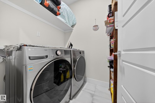 Dedicated laundry area featuring a front-loading washer and dryer, white shelving, built-in wooden shelving, white walls, and a white paneled door - 449 Roberts Cres, Leduc, AB 