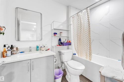 Bathroom featuring a light gray vanity with an integrated sink, a contemporary framed mirror, a full bathtub with a tiled surround, and wood-finish flooring - 449 Roberts Cres, Leduc, AB 