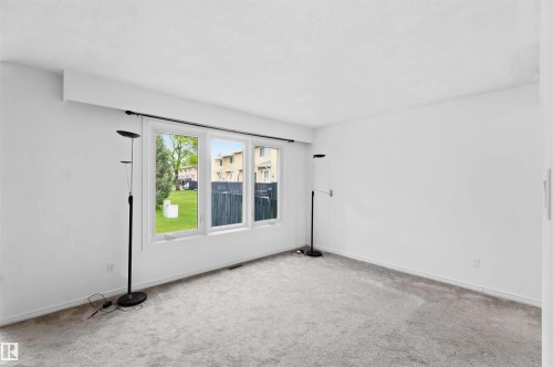 Room featuring light gray carpet, white painted walls, and a multi-pane window overlooking a green lawn - 17325 85 Avenue Nw, Edmonton, AB 