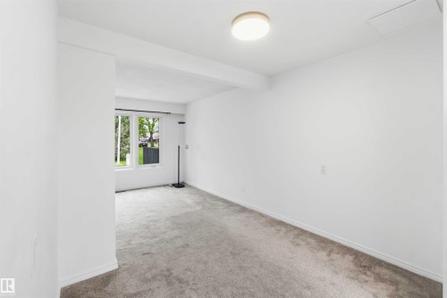 Bright interior room with white walls, grey carpet flooring, and a flush-mount ceiling light fixture - 17325 85 Avenue Nw, Edmonton, AB 