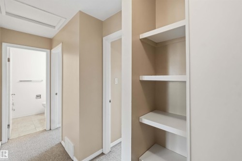 Hallway featuring neutral wall paint, white trim, carpet flooring, a visible attic access panel, and built-in shelving - 17325 85 Avenue Nw, Edmonton, AB 