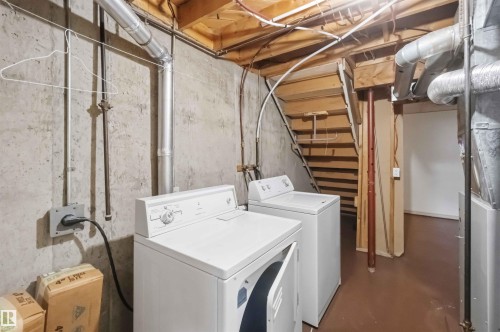 Utility space featuring a washer and dryer, exposed concrete walls, and wood-finish stairs - 17325 85 Avenue Nw, Edmonton, AB 