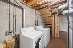 Utility space featuring a washer and dryer, exposed concrete walls, and wood-finish stairs - 
