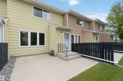 Rear exterior patio with concrete surfacing and black picket fencing, featuring light yellow siding and white window frames - 
