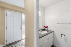 Entryway featuring a paneled door with frosted sidelight, wood-finish flooring, and a powder room with a vanity sink and dark countertop - 