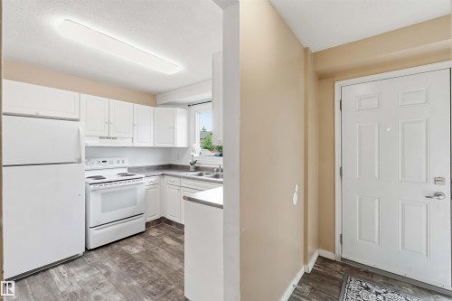 Kitchen featuring white cabinetry, white appliances, wood-finish flooring, and a window - 17325 85 Avenue Nw, Edmonton, AB 