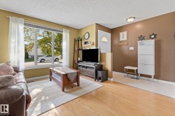 Living area featuring wood-finish flooring, a large multi-pane window, and a white entry door with an arched glass insert - 