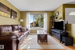 Living room featuring wood-finish flooring, a large window with white trim, and a built-in wall shelf - 