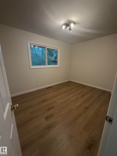 Bedroom featuring wood-finish flooring, a window with exterior tree scenery, a ceiling-mounted track light fixture, and light-toned wall finishes - 9640 74 Avenue, Edmonton, AB 
