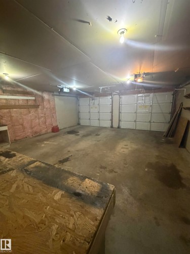 Two-car garage featuring concrete flooring, exposed insulation, overhead lighting, and two individual garage doors - 9640 74 Avenue, Edmonton, AB 