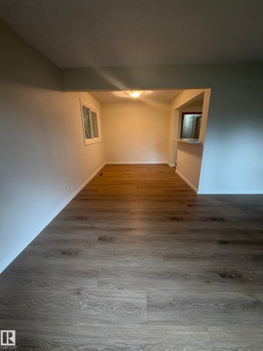 Spacious interior featuring wood-finish flooring, a pass-through counter, and a window - 9640 74 Avenue, Edmonton, AB 