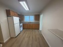 Kitchen featuring wood-finish flooring, light wood cabinetry, white appliances, and a window with horizontal blinds - 9640 74 Avenue, Edmonton, AB 