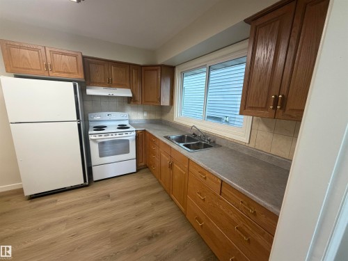 Kitchen featuring wood-finish cabinetry, a double basin stainless steel sink, and light-toned wood-finish flooring - 9640 74 Avenue, Edmonton, AB 