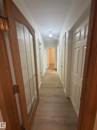 Hallway featuring wood-finish flooring, white paneled doors, and a decorative flush-mount ceiling light - 9640 74 Avenue, Edmonton, AB 