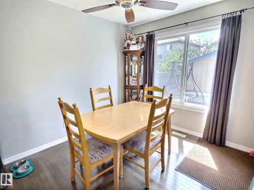 Dining area featuring wood-finish flooring, a ceiling fan with integrated lighting, and a large window with white trim - 126 Calvert Wynd, Fort Saskatchewan, AB 