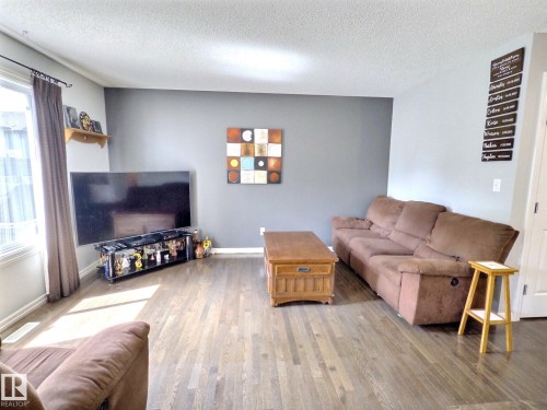Spacious room featuring wood-finish flooring, a large window, and light gray walls with a contrasting accent wall - 126 Calvert Wynd, Fort Saskatchewan, AB 