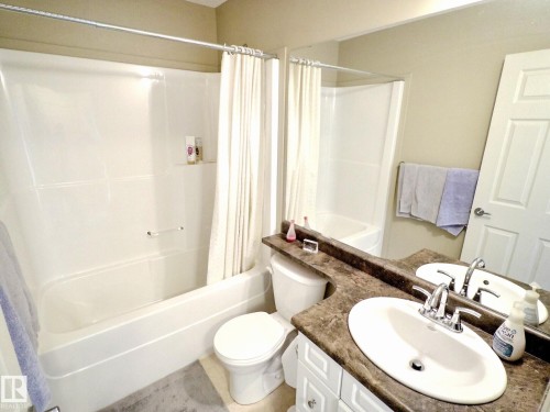 Bathroom featuring a white bathtub/shower combination, a vanity with a dual sink, a brown patterned countertop, white cabinetry, and a full-width mirror - 126 Calvert Wynd, Fort Saskatchewan, AB 
