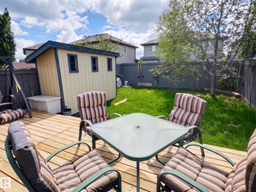 Expansive wood deck with a privacy fence, a detached shed featuring multiple windows, and a grassy yard with mature trees - 126 Calvert Wynd, Fort Saskatchewan, AB 