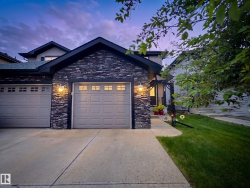 Contemporary exterior featuring stacked stone accents, two paneled garage doors with upper window inserts, and a concrete driveway - 126 Calvert Wynd, Fort Saskatchewan, AB 