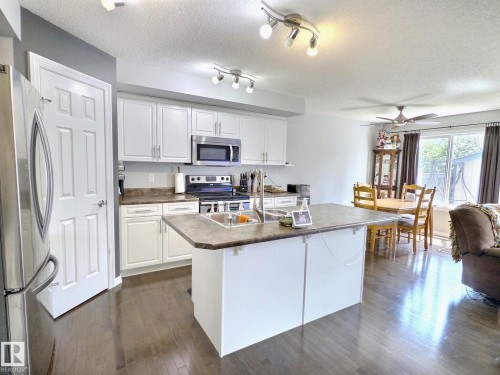 Kitchen featuring wood-finish flooring, white cabinetry, stainless steel appliances, and a central island with an integrated sink - 126 Calvert Wynd, Fort Saskatchewan, AB 