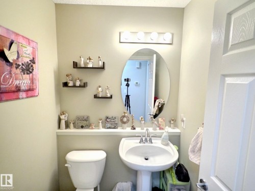 Pedestal sink with chrome faucet, oval mirror, and three-bulb vanity light fixture - 126 Calvert Wynd, Fort Saskatchewan, AB 