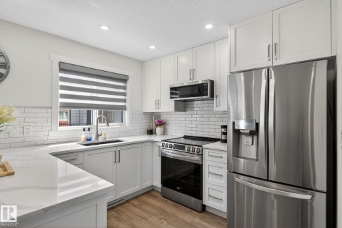 Kitchen featuring light wood-finish flooring, white subway tile backsplash, light stone countertops, light gray lower cabinetry, and white upper cabinetry - 16 9250 156 Avenue, Edmonton, AB 