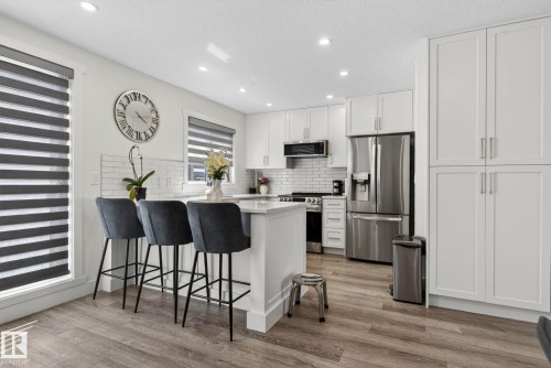 Contemporary kitchen featuring an island with seating, white shaker cabinetry, stainless steel appliances, a white subway tile backsplash, and wood-finish flooring - 16 9250 156 Avenue, Edmonton, AB 