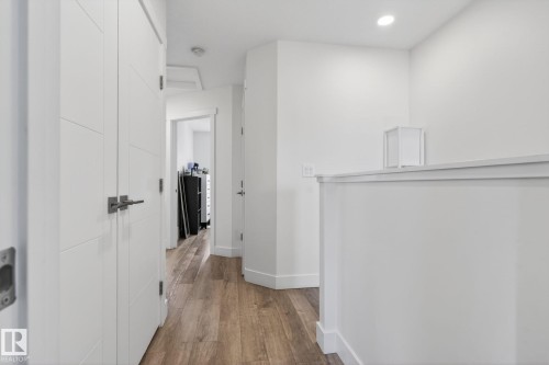 Hallway featuring wood-finish flooring, recessed lighting, white paneled doors with contemporary hardware, and white baseboards - 16 9250 156 Avenue, Edmonton, AB 
