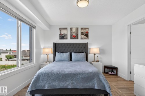 Bedroom featuring a large window, a tufted headboard, wood-finish flooring, a flush-mount ceiling light, and white walls - 16 9250 156 Avenue, Edmonton, AB 