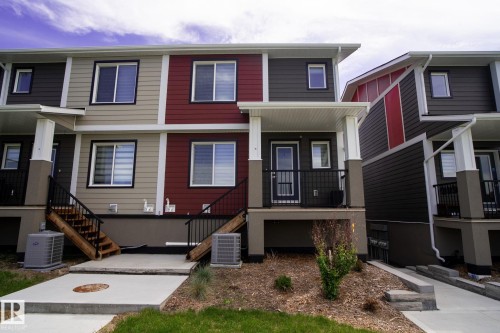 Multi-level townhouse exterior featuring contrasting siding colors, multiple windows, covered porch entries with black metal railings, and concrete walkways - 16 9250 156 Avenue, Edmonton, AB 