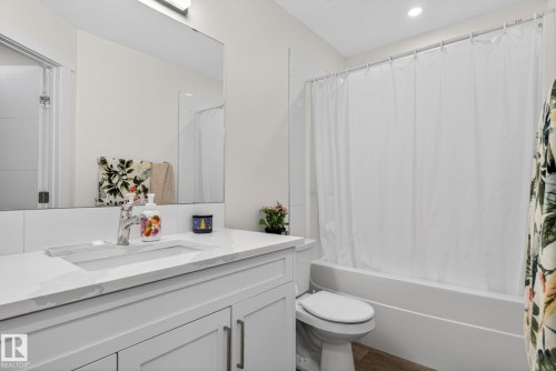 Bathroom featuring a vanity with a white countertop and integrated rectangular sink, a large wall-mounted mirror, a tub/shower combination with white subway tile surround, and wood-finish flooring - 16 9250 156 Avenue, Edmonton, AB 
