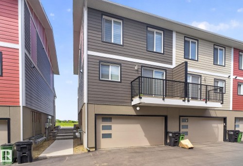 Modern townhome exterior featuring multi-toned siding, a second-story balcony with black railings, and an integrated garage with a contemporary door design - 16 9250 156 Avenue, Edmonton, AB 