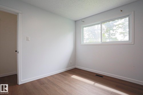 Light-filled room featuring wood-finish flooring, white baseboards, and a large sliding window - 10 Murray Crescent, St. Albert, AB 