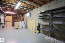 Unfinished basement featuring exposed joists, concrete walls, painted concrete flooring, and ample storage shelving - 