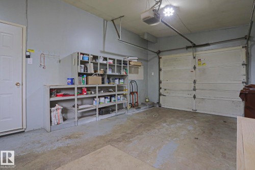 Spacious garage with an overhead door, concrete flooring, built-in shelving, and direct interior access - 10 Murray Crescent, St. Albert, AB 