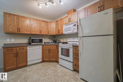 Compact kitchen featuring wood-finish cabinetry, a white refrigerator, and an electric range with an overhead microwave - 119 309 Clareview Station Drive, Edmonton, AB 