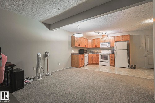 Combined living area featuring a kitchen with wood-finish cabinetry, white appliances, and laminate flooring - 119 309 Clareview Station Drive, Edmonton, AB 