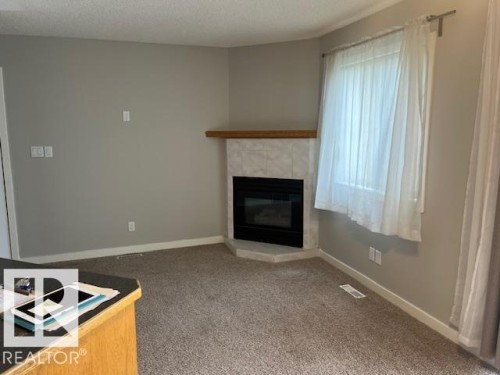 Corner fireplace featuring a tile surround and wood mantel - 16-1033 Youville Dr. West Nw, Edmonton, AB - Indoor Photo Showing Living Room With Fireplace