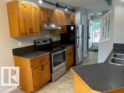 Kitchen featuring wood-finish cabinetry, dark countertops, a stainless steel refrigerator, and a stainless steel range with overhead ventilation - 