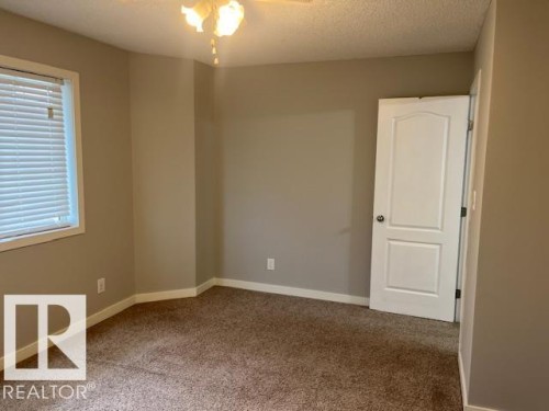 Carpeted room featuring a window with horizontal blinds, a white paneled door, neutral wall paint, white baseboards, and a ceiling fan with light fixture - 16-1033 Youville Dr. West Nw, Edmonton, AB - Indoor Photo Showing Other Room