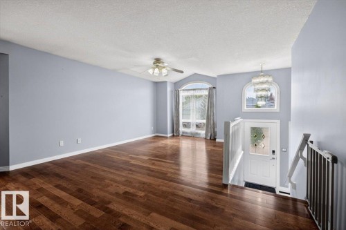 Spacious room featuring wood-finish flooring, a contemporary ceiling fan, and a large arched window with drapery - 946 Jordan Crescent, Edmonton, AB 