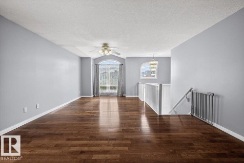 Hardwood-finish flooring extends throughout this spacious room, featuring light gray walls and white trim - 946 Jordan Crescent, Edmonton, AB 