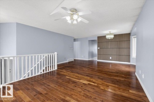 Spacious interior featuring wood-finish flooring, a contemporary accent wall with vertical slat detailing, and a multi-light ceiling fan - 946 Jordan Crescent, Edmonton, AB 