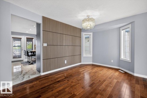 Hardwood flooring in a spacious room featuring a decorative slatted accent wall and a contemporary chandelier - 946 Jordan Crescent, Edmonton, AB 