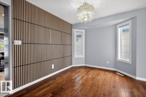 Room featuring a wood-panel accent wall, rich wood-finish flooring, and a decorative ceiling light fixture - 946 Jordan Crescent, Edmonton, AB 