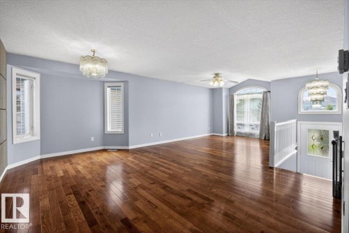 Open concept living area featuring wood-finish flooring, multiple windows with white plantation shutters, and a decorative ceiling light fixture - 946 Jordan Crescent, Edmonton, AB 