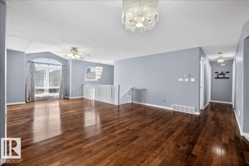 Spacious living area featuring polished wood-finish flooring, an arched window, and a white spindle railing - 946 Jordan Crescent, Edmonton, AB 