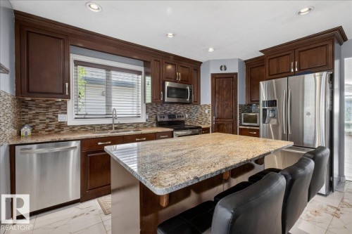 Kitchen featuring dark wood cabinetry, stainless steel appliances, a tile backsplash, light-toned granite countertops, and recessed lighting - 946 Jordan Crescent, Edmonton, AB 