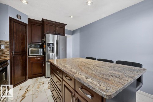 Kitchen featuring a large central island with a stone countertop, recessed lighting, ample cabinetry, and stainless steel appliances including a refrigerator - 946 Jordan Crescent, Edmonton, AB 
